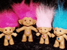 four troll dolls with pink , white and blue hair are standing next to each other .