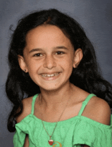 a young girl wearing a green off the shoulder top and a necklace smiles for the camera