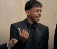 a man in a suit and bow tie is smiling and giving the middle finger .