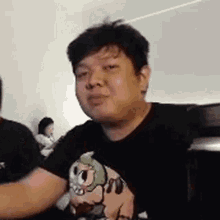 a man in a black t-shirt is making a funny face while sitting at a table .