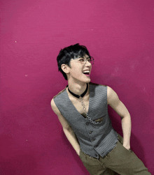 a young man wearing glasses and a choker is laughing in front of a pink wall