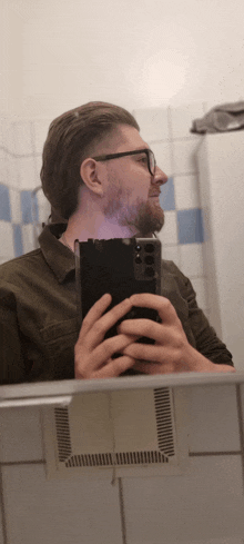 a man with glasses is taking a selfie in a bathroom mirror