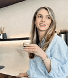 a woman in a blue shirt is holding a cup of coffee .