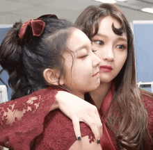 two girls hugging each other with one wearing a red lace dress