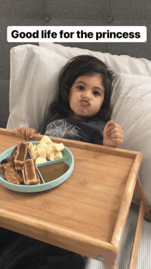 a little girl is sitting on a bed with a plate of food and the words good life for the princess