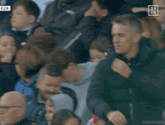 a man in a black jacket stands in a crowd with a da za logo on the bottom