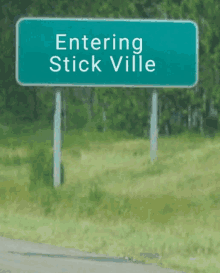 a green road sign says entering stick ville