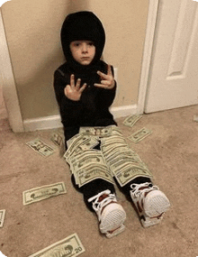 a little boy in a hooded jacket is sitting on the floor with money wrapped around his legs .