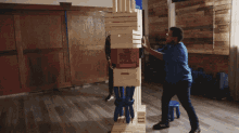 a man in a blue shirt is standing next to a stack of wooden crates one of which has a red crate on it