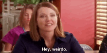 a woman is sitting at a table in a restaurant and saying `` hey , weirdo . ''