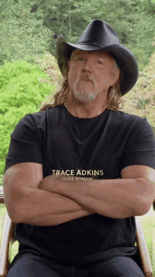 a man wearing a black shirt that says trace adkins is sitting in a chair with his arms crossed