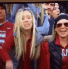 a group of people are sitting in a stadium watching a game and one of them is wearing sunglasses .