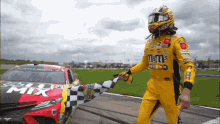 a race car driver is waving a checkered flag in front of a race car sponsored by m & m 's .