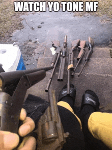 a person is holding a gun in front of a bunch of guns and the caption says watch yo tone mf