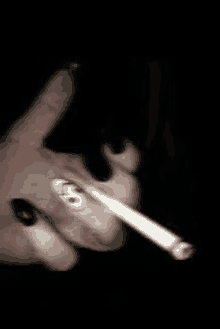 a person with black nails is smoking a cigarette in a dark room .