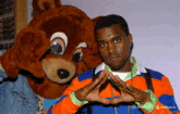 a man in an orange and blue striped sweater stands next to a teddy bear