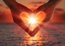 a person making a heart shape with their hands in front of a sunset over the ocean