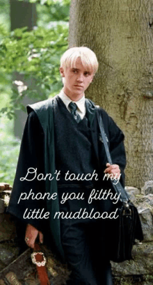 a harry potter character is standing next to a tree holding a briefcase and a phone .