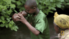 a boy in a green shirt is playing a musical instrument next to a woman in a yellow head scarf and a national geographic logo