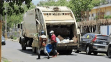 a garbage truck is parked on the side of the road and people are walking towards it .