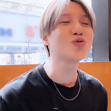 a young man wearing a black t-shirt and a silver chain around his neck is making a funny face