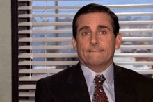 a man in a suit and tie is sitting in front of a window with blinds on it