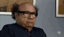 a bald man wearing glasses is sitting in front of a wall .