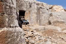 a group of people are sitting in a cave in the middle of a rocky mountain .