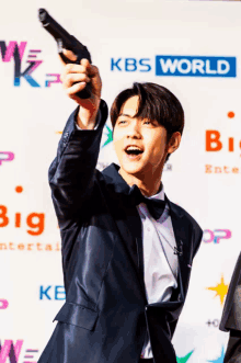 a man in a suit and bow tie is holding a gun in front of a kbs world sign