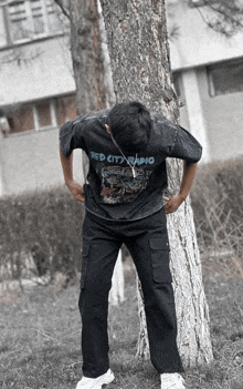 a man leaning against a tree wearing a red city radio t-shirt