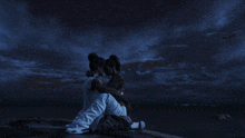 a man and woman are sitting on a rock under a starry night sky