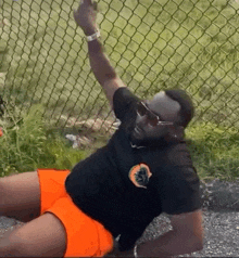 a man is laying on the ground next to a chain link fence wearing orange shorts and sunglasses .