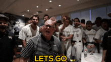 a man in a striped shirt stands in front of a group of baseball players with the words let 's go on the bottom right