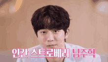 a close up of a young man 's face with a pink background and korean writing .