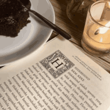 a piece of cake sits on a plate next to a book and a candle