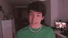 a young man wearing a green shirt and a pearl necklace is smiling