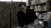 a man in a suit and tie is standing in a room with a shelf filled with boxes .