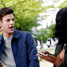 a man in a blue jacket is talking to a woman in a park .