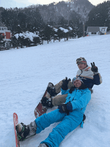 a man and a woman are laying in the snow on a snowboard