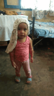 a little girl wearing a pink tank top and pink pants is standing in front of a bed