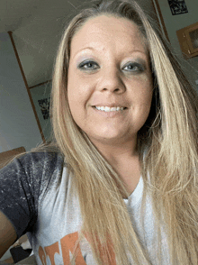 a woman with long blonde hair is smiling and wearing a t-shirt that says " i love you "