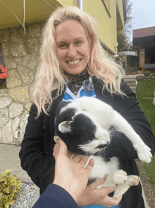 a woman is holding a black and white cat and smiling