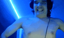 a shirtless man wearing headphones is smiling in front of a blue background