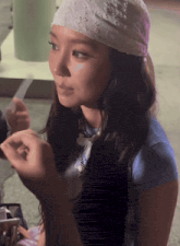 a woman wearing a bandana and a blue shirt is applying makeup to her face