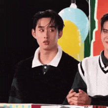a young man is sitting next to another young man in front of a balloon .