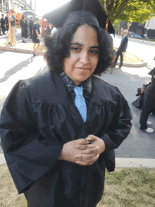 a woman wearing a graduation cap and gown stands with her hands folded