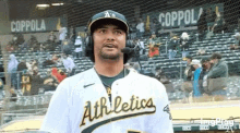 a baseball player wearing headphones and a microphone is standing in front of a crowd at a baseball game .