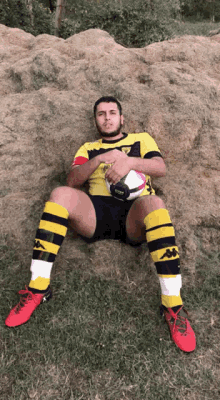 a man in a yellow and black shirt is sitting on a pile of hay holding a soccer ball ..