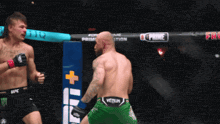 two men are fighting in a cage and one of them is wearing green shorts that say venum