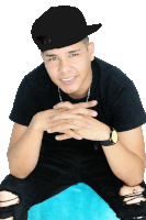 a young man wearing a black shirt and a black hat is sitting with his hands folded